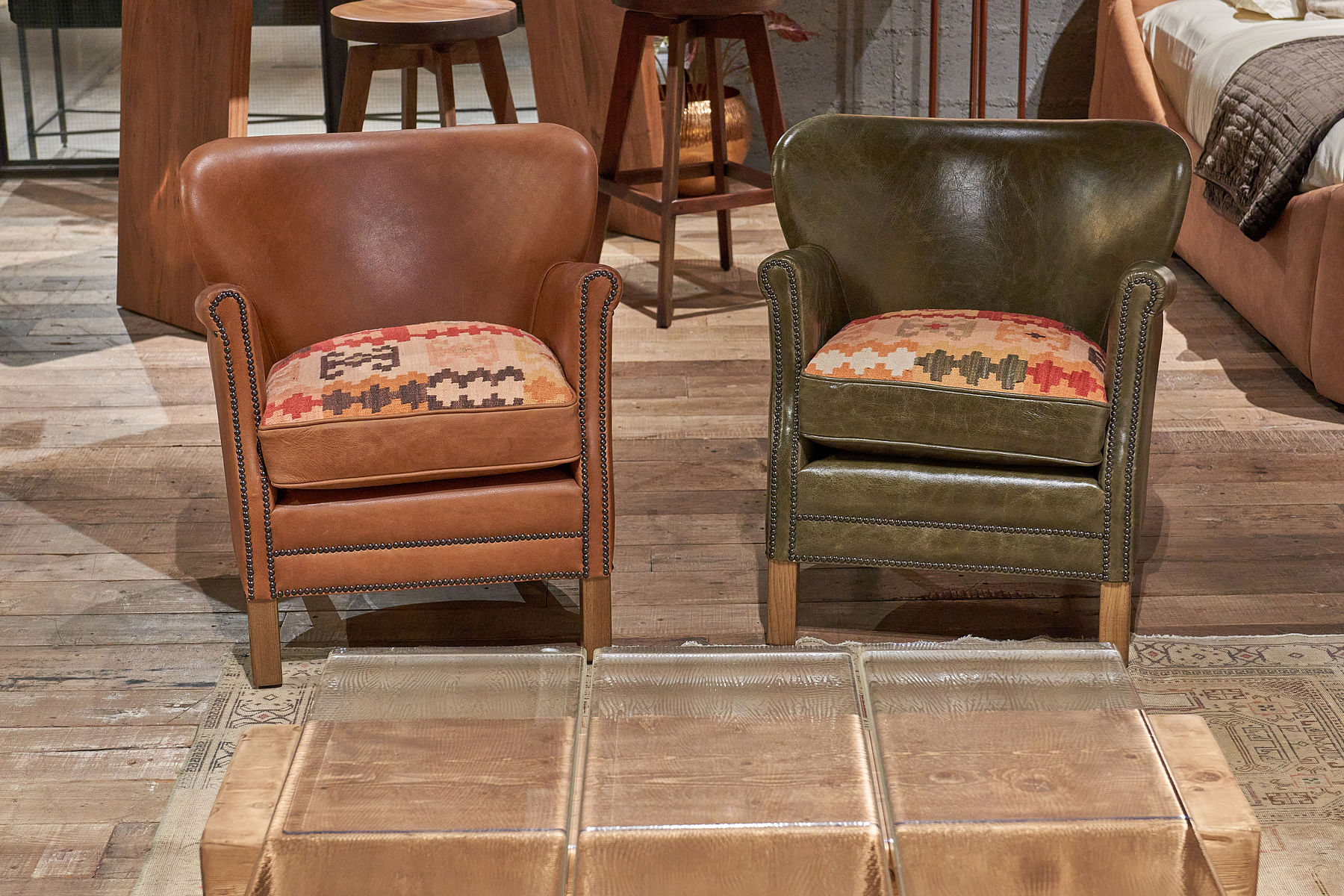 Two leather armchairs in green and brown feature tribal fabric seats and wooden legs.