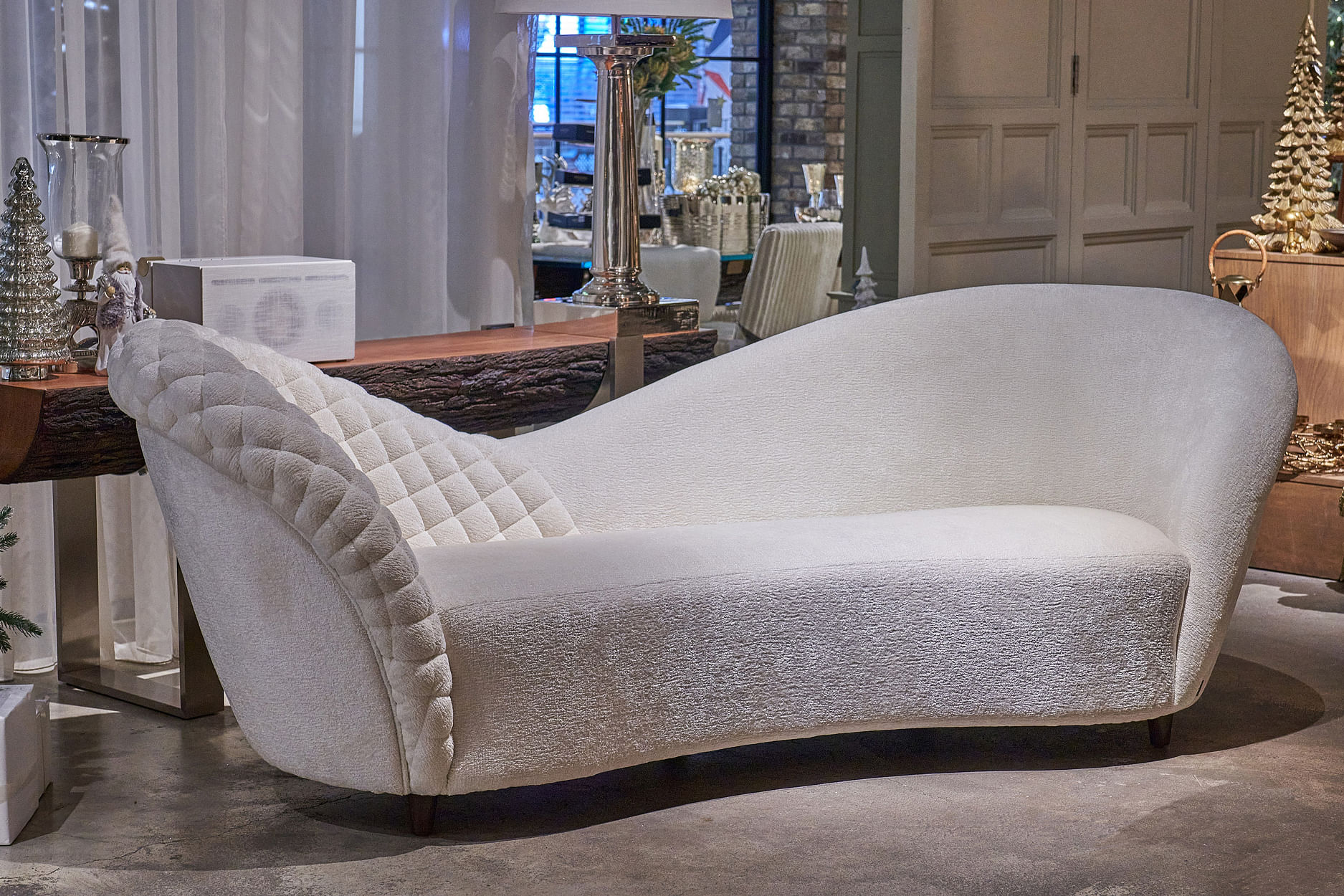 A quilted pearl-hued chaise longue sits in front of a console.